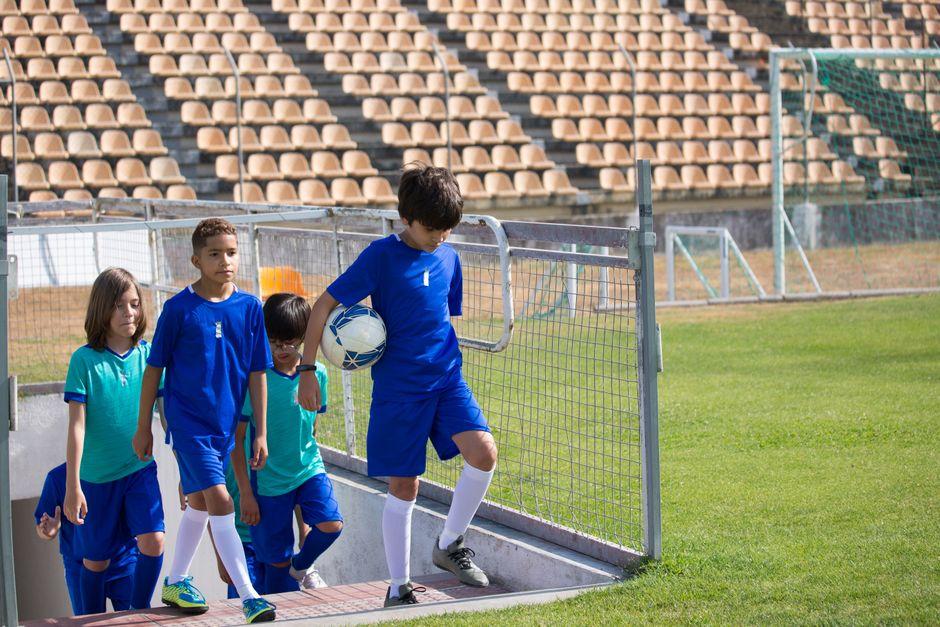 A group of children in blue uniforms entering a soccer field, carrying a ball.