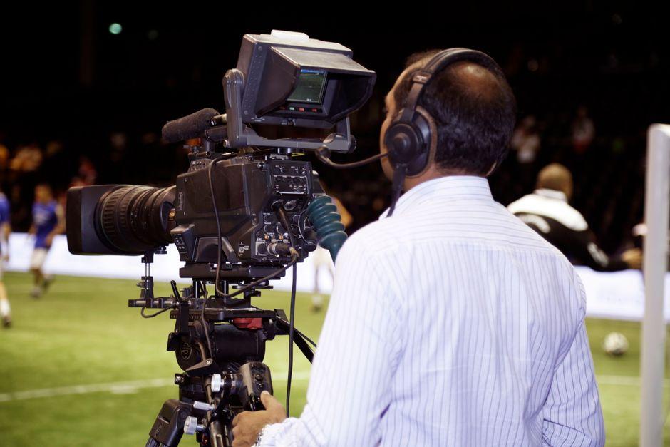 A cameraman filming a soccer match in a stadium, capturing the action on video.
